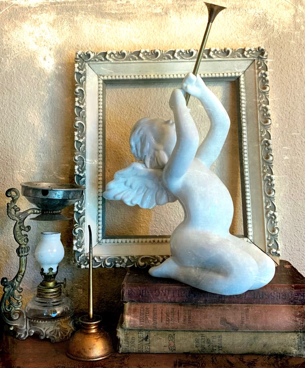 Vintage sculpture of a figure with a trumpet, antique books, and ornate frame, evoking classic artistic decor.