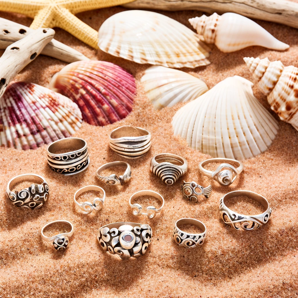 A collection of vintage silver rings displayed on a rustic wooden surface, intertwined with vibrant summer fabrics, showcasing the cool, versatile appeal of these accessories for enhancing any summer outfit.